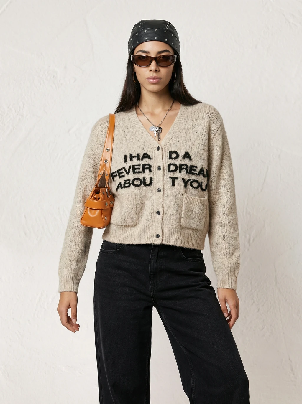 AI model in a beige slogan cardigan, black jeans, studded bandana and orange shoulder bag, generated with Veeton