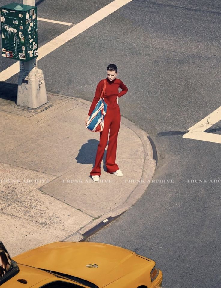 Model in a red turtleneck and flared trousers with a Union Jack tote standing on a New York street corner