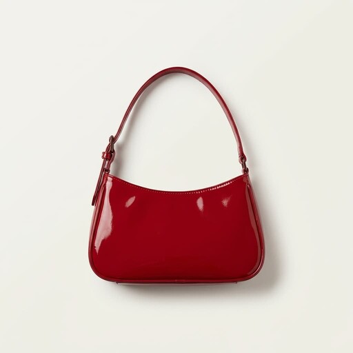 A glossy red handbag with a curved silhouette, featuring a single strap and sleek, minimalist design, set against a plain white background.