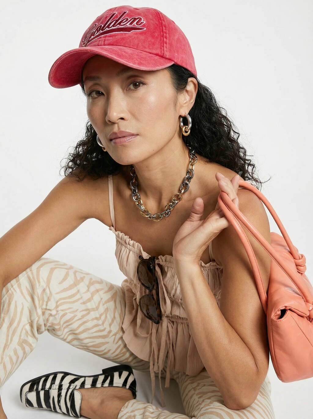 AI model seated with a coral bag wearing a washed red Golden baseball cap, generated with Veeton