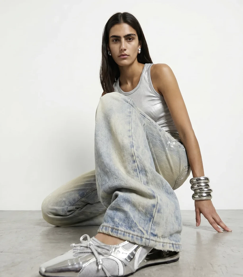 AI model in a silver tank top, washed jeans and metallic sneakers seated on a studio floor, generated with Veeton