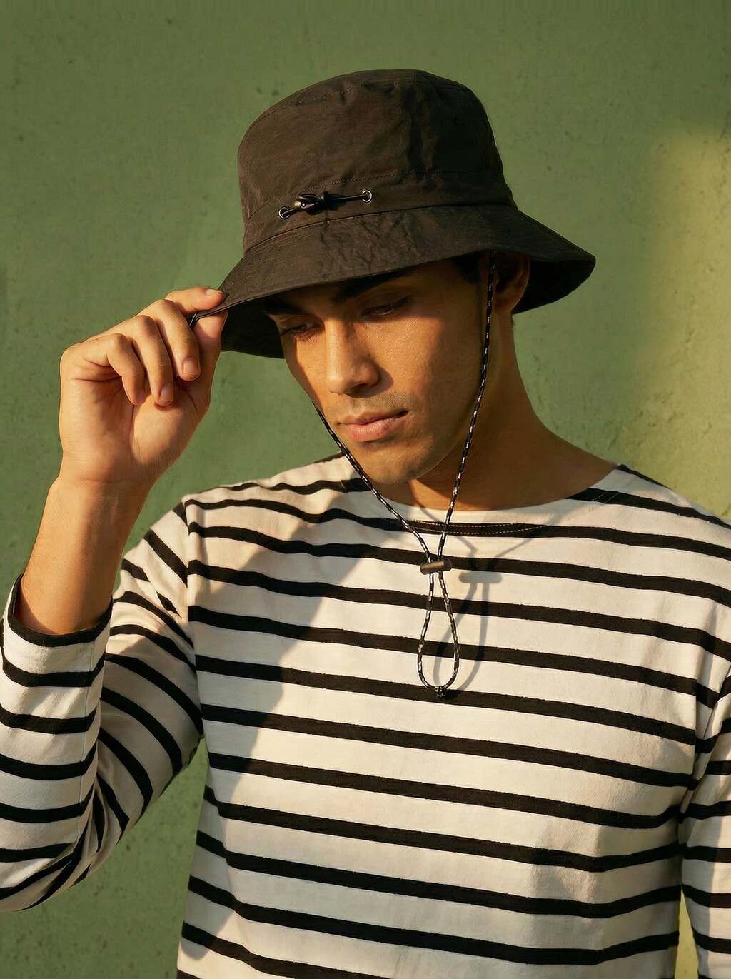 AI model in a striped Breton top tipping a black bucket hat against a green wall, generated with Veeton