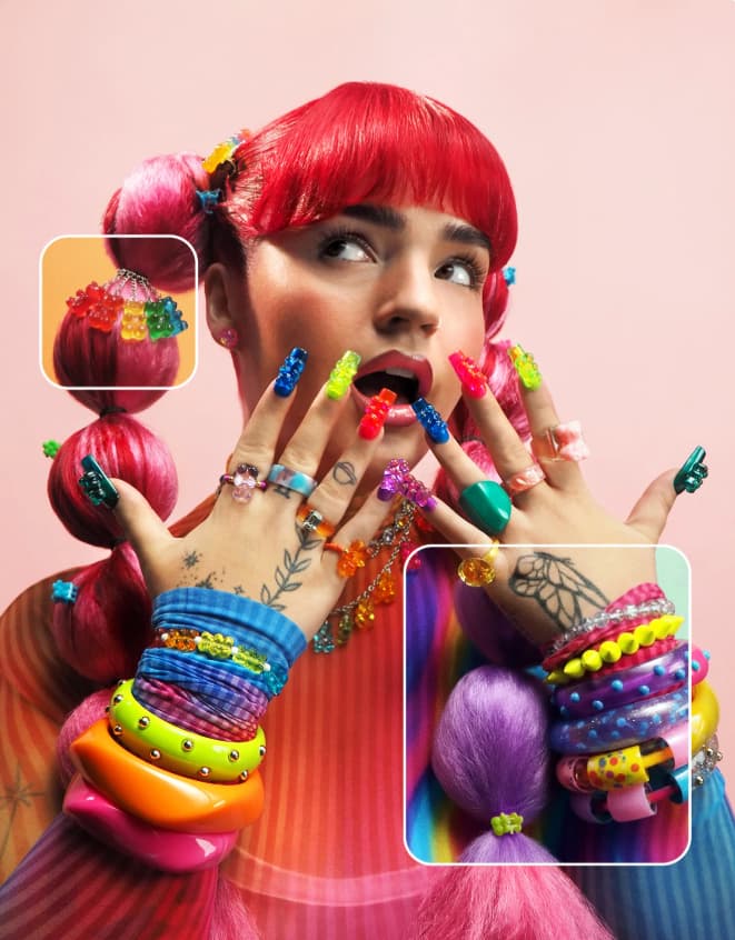 Red-haired model with rainbow stacked bracelets, gummy-bear nails and candy hair clips on a pink background