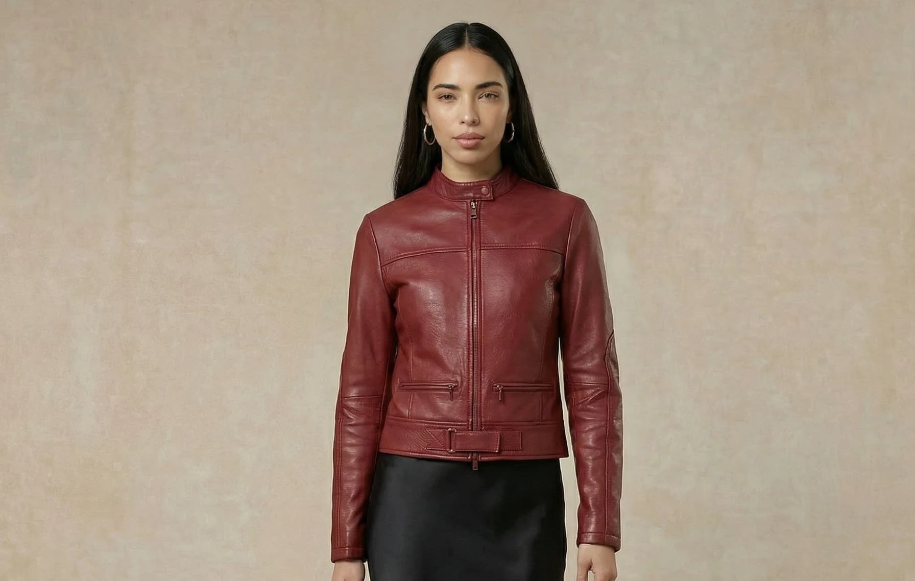 Model in a burgundy leather biker jacket and black skirt against a beige textured backdrop