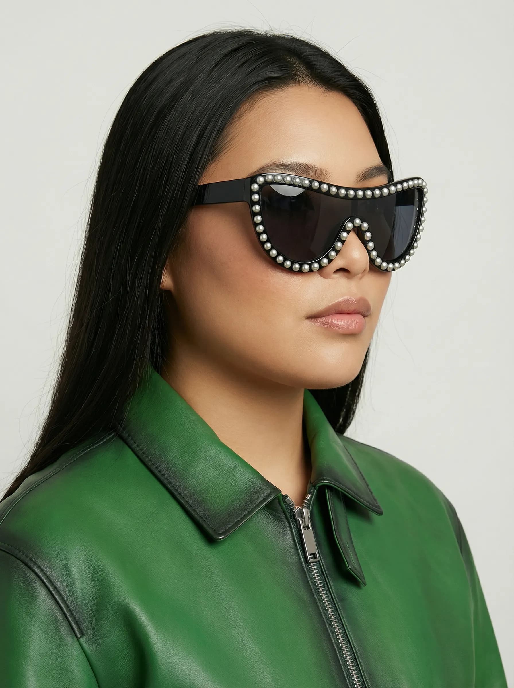 Model in a green leather jacket wearing black pearl-trimmed shield sunglasses