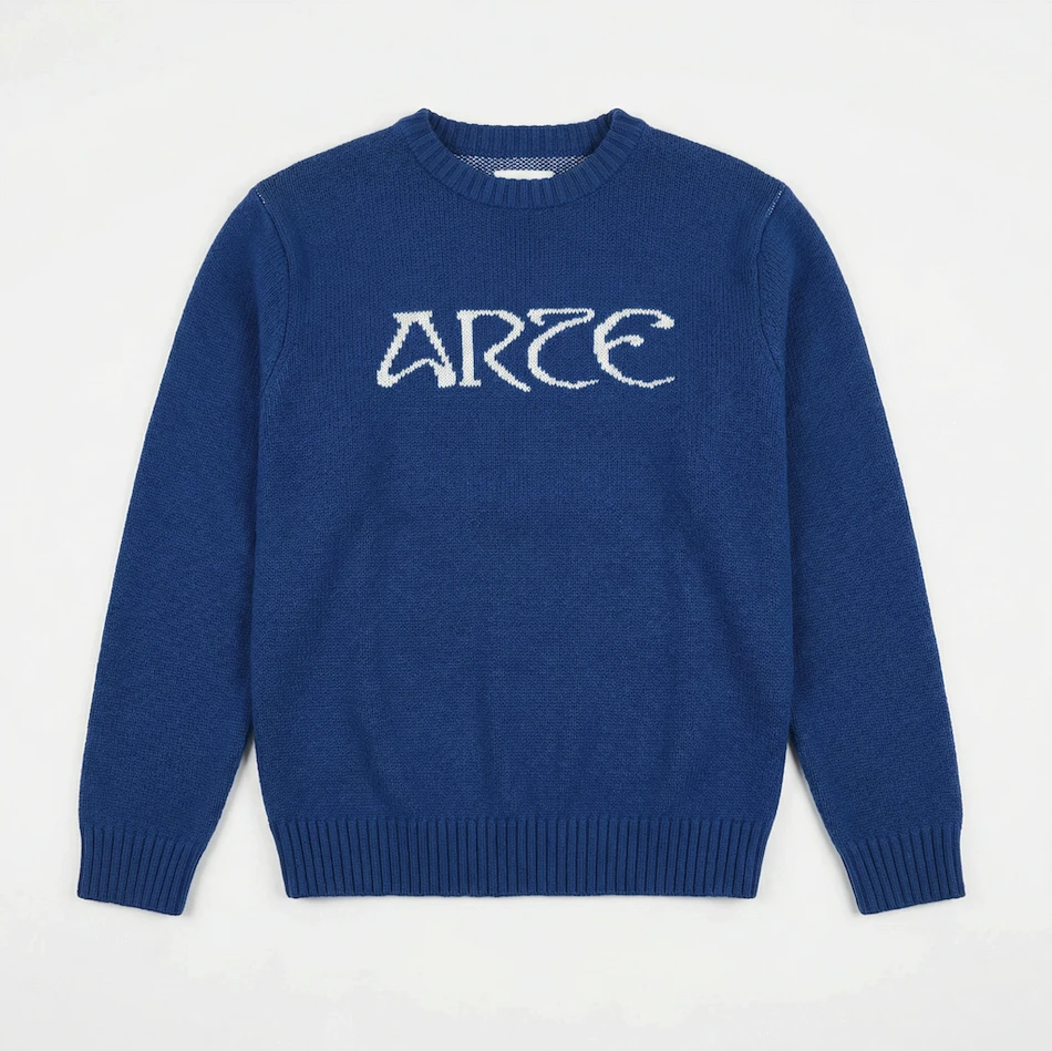 Flat lay of a royal blue knit sweater with white 'ARTE' lettering on a white background