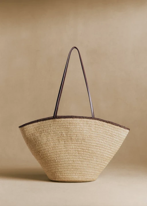Packshot of a woven straw tote bag with brown leather handles