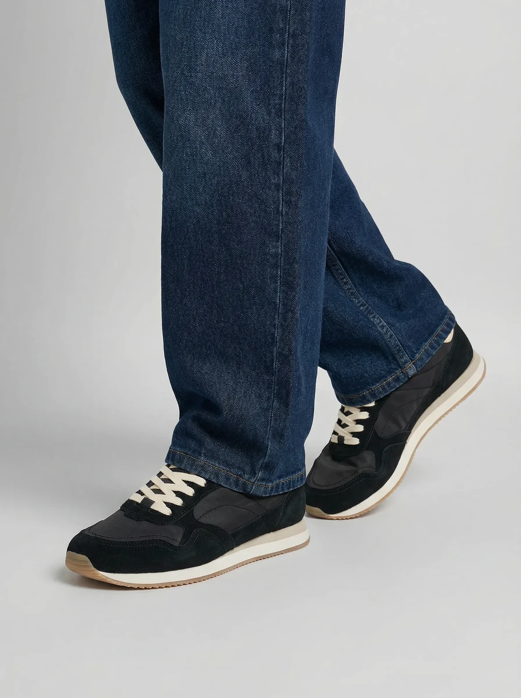 AI model in blue jeans wearing black suede retro sneakers with cream laces, generated with Veeton