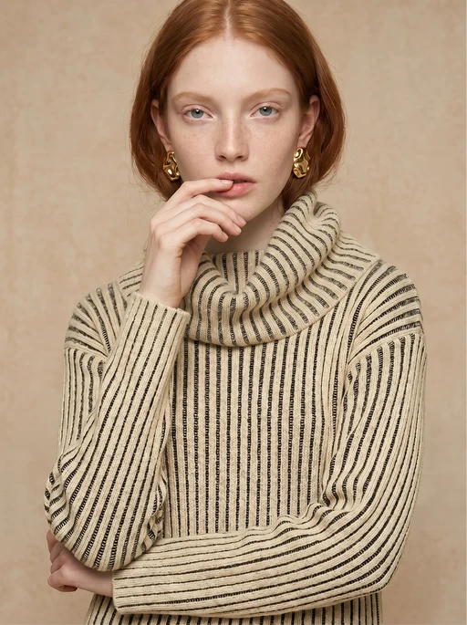Red-haired AI model in a cream and black ribbed turtleneck knit, hand raised to her lips, front view close-up