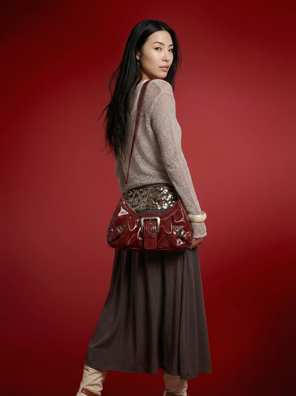 AI model in a knit top and grey skirt carrying a burgundy patent shoulder bag on a red background, generated with Veeton