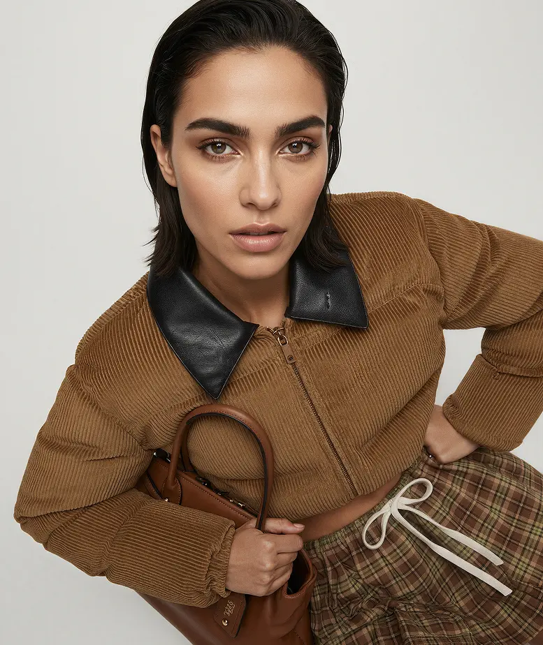 AI model in a tan corduroy jacket with black leather collar holding a brown bag, generated with Veeton